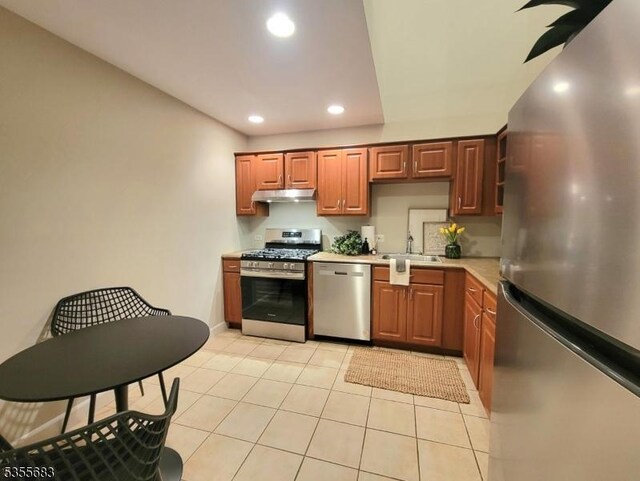 kitchen featuring appliances with stainless steel finishes, under cabinet range hood, a sink, light countertops, and recessed lighting