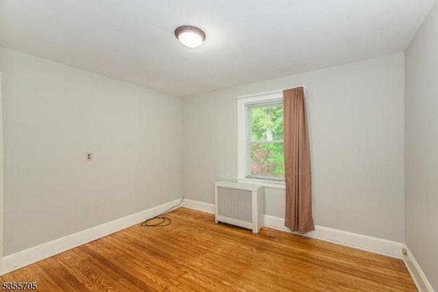 empty room with radiator heating unit, baseboards, and light wood finished floors