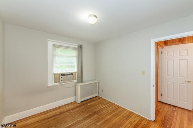 empty room featuring radiator heating unit, cooling unit, light wood-type flooring, and baseboards