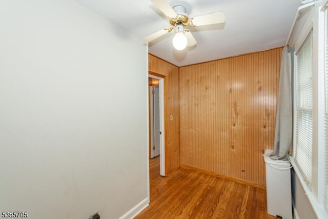 unfurnished room featuring baseboards, wood finished floors, wood walls, and ceiling fan