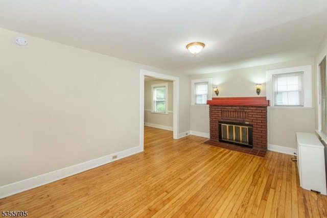 unfurnished living room with a brick fireplace, light wood-type flooring, and baseboards