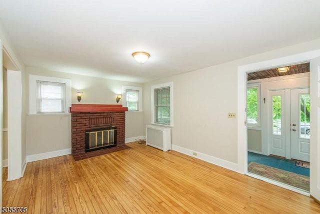 unfurnished living room featuring light wood-type flooring, baseboards, and a brick fireplace