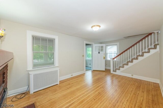 unfurnished living room featuring radiator, stairs, wood finished floors, and baseboards