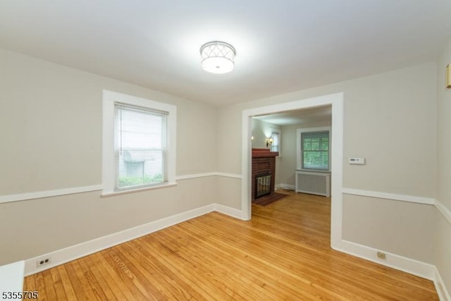empty room with light wood-type flooring, a brick fireplace, and baseboards
