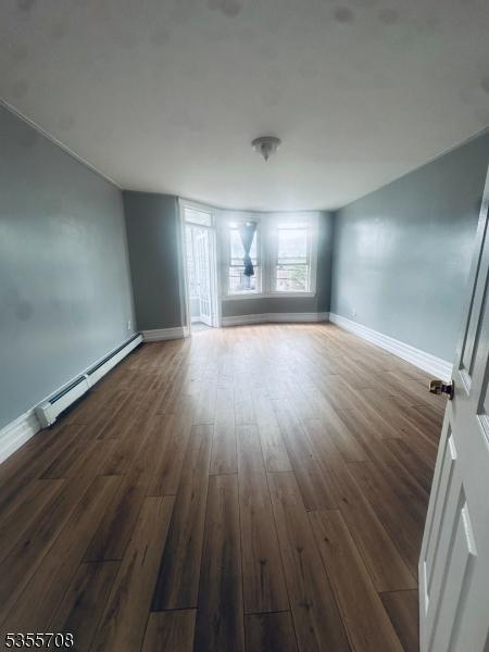 553-555 S 10th St, Newark City, NJ 07103 - empty room with wood finished floors, a baseboard heating unit, and baseboards