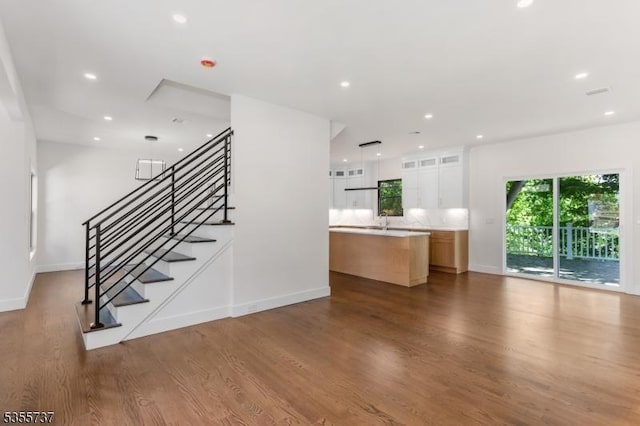 unfurnished living room featuring baseboards, wood finished floors, recessed lighting, stairs, and a sink