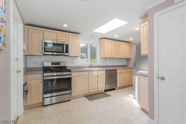 kitchen featuring appliances with stainless steel finishes, light brown cabinets, a sink, a skylight, and light countertops