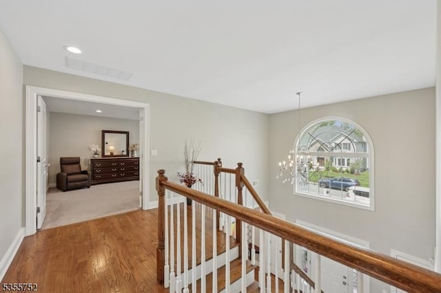 hallway with an upstairs landing, wood finished floors, a chandelier, and baseboards