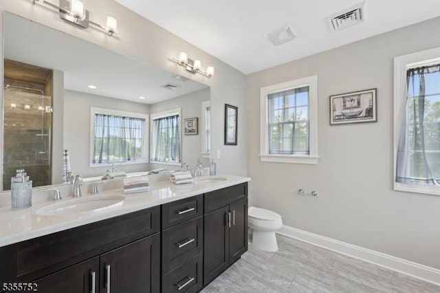 bathroom with plenty of natural light, double vanity, tiled shower, and baseboards