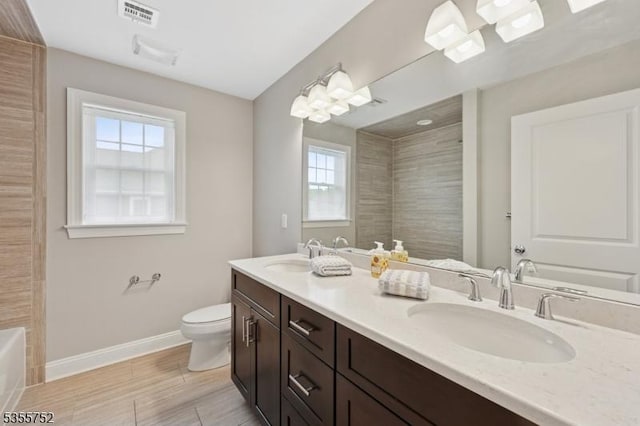 bathroom featuring baseboards, a bath, toilet, double vanity, and wood finished floors