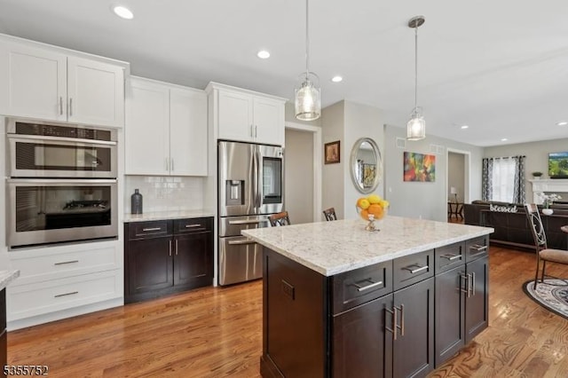 kitchen featuring appliances with stainless steel finishes, white cabinets, light wood finished floors, open floor plan, and hanging light fixtures