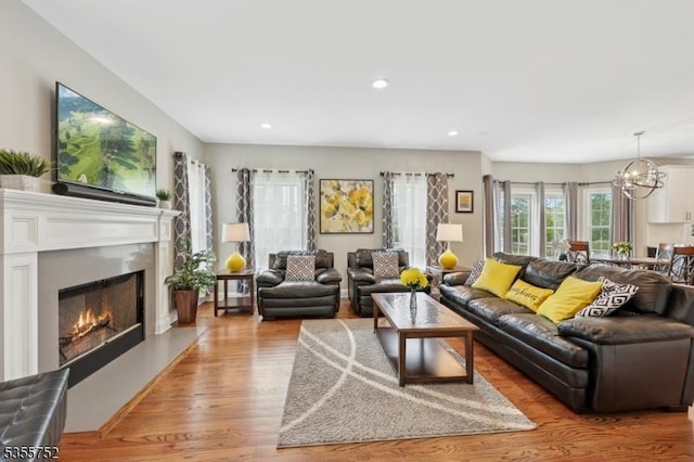 living room with light wood-style floors, a lit fireplace, a chandelier, and recessed lighting