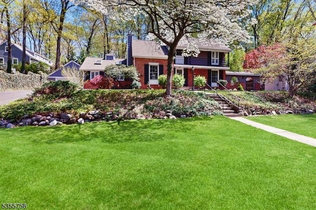 view of front of home with a chimney, stairway, brick siding, and a front lawn