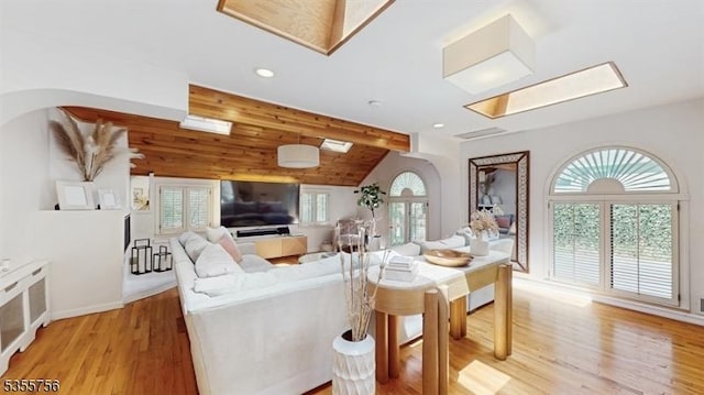living room featuring light wood-style flooring, recessed lighting, baseboards, arched walkways, and vaulted ceiling with skylight