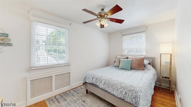 bedroom with multiple windows, wood finished floors, and baseboards