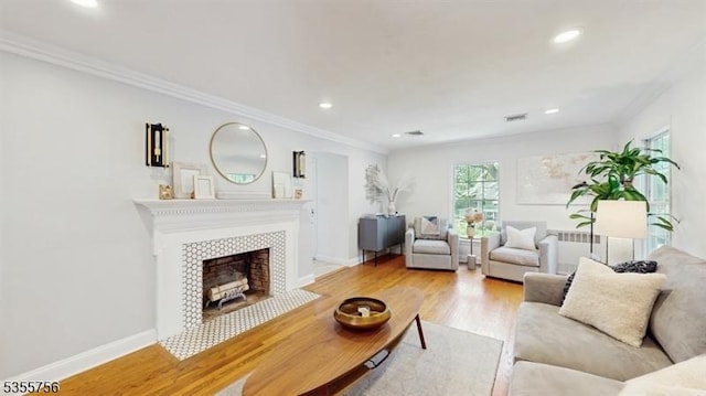 living room with wood finished floors, a tiled fireplace, visible vents, ornamental molding, and recessed lighting
