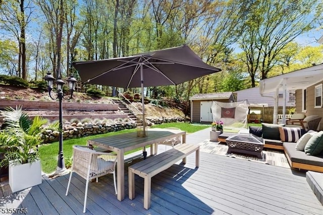 wooden deck featuring outdoor dining space, a storage unit, fence, an outdoor living space with a fire pit, and an outbuilding