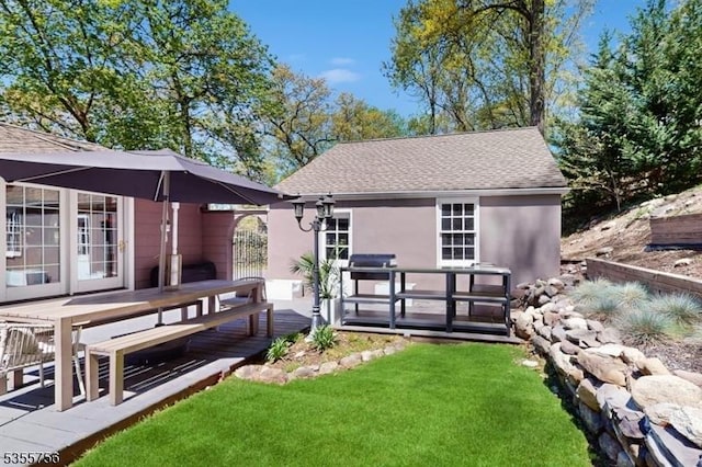 back of property with a yard, stucco siding, roof with shingles, and a wooden deck