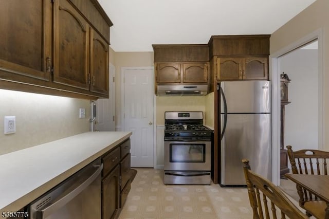 kitchen with appliances with stainless steel finishes, under cabinet range hood, light countertops, and light floors