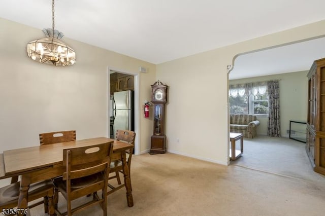 dining area featuring a chandelier, light carpet, and baseboards
