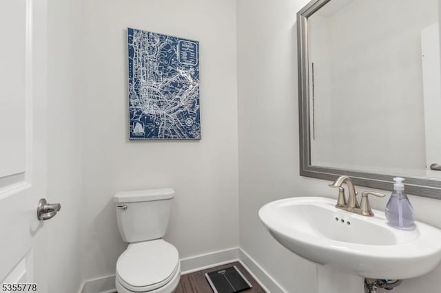 half bathroom featuring toilet, baseboards, wood finished floors, and a sink
