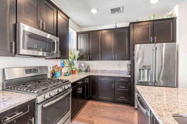 kitchen with appliances with stainless steel finishes, visible vents, light stone counters, and dark brown cabinets