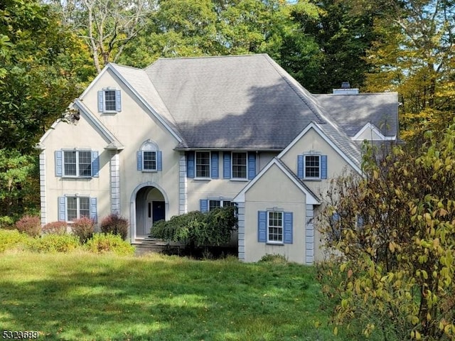 view of front of home featuring central air condition unit, roof with shingles, stucco siding, a front yard, and a chimney