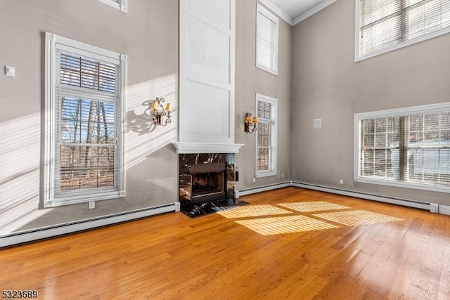 unfurnished living room with a premium fireplace, a baseboard radiator, ornamental molding, a towering ceiling, and wood finished floors
