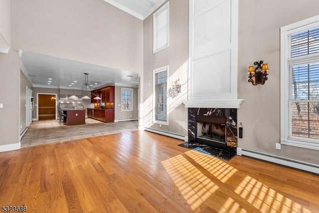 unfurnished living room with crown molding, a high end fireplace, baseboard heating, and light wood-type flooring