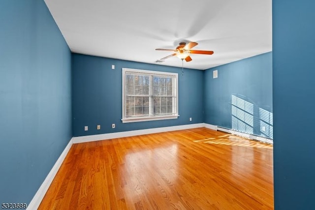 empty room with baseboard heating, wood finished floors, baseboards, and ceiling fan