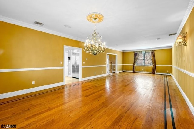 spare room with an inviting chandelier, wood finished floors, visible vents, baseboards, and ornamental molding