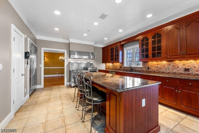 kitchen featuring wall chimney range hood, ornamental molding, backsplash, a center island, and stainless steel built in fridge