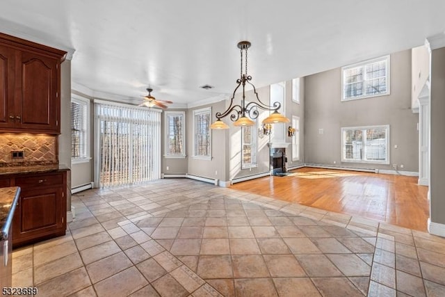 unfurnished dining area featuring baseboards, baseboard heating, a fireplace, and ceiling fan with notable chandelier