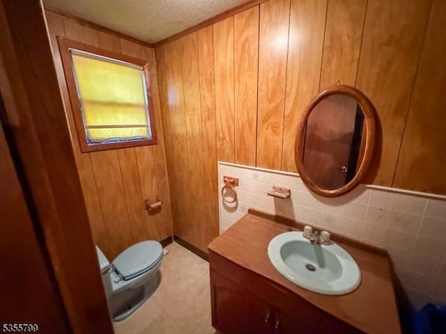 bathroom with a textured ceiling, toilet, backsplash, vanity, and wood walls