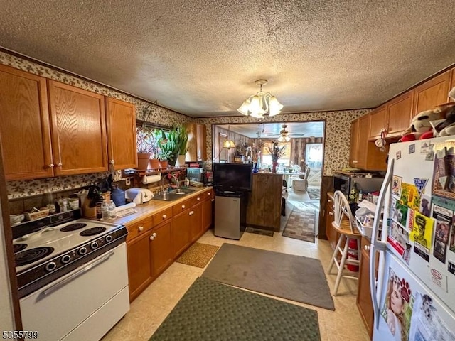 kitchen featuring white appliances, brown cabinets, a chandelier, light floors, and wallpapered walls