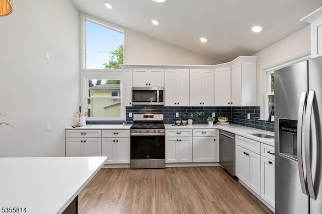 kitchen with stainless steel appliances, decorative backsplash, vaulted ceiling, light countertops, and white cabinets
