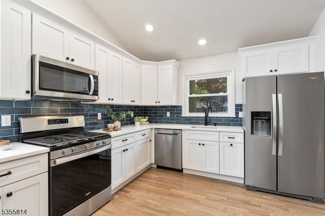 kitchen with appliances with stainless steel finishes, a sink, light countertops, white cabinetry, and light wood-type flooring