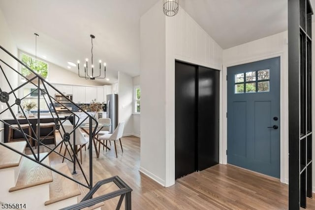 entryway with light wood-type flooring, a chandelier, stairs, high vaulted ceiling, and healthy amount of natural light