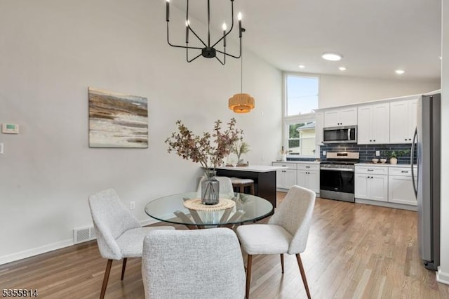 dining area featuring light wood-type flooring, a chandelier, baseboards, and high vaulted ceiling