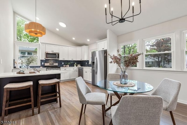 dining area featuring a chandelier, light wood-style flooring, recessed lighting, and high vaulted ceiling