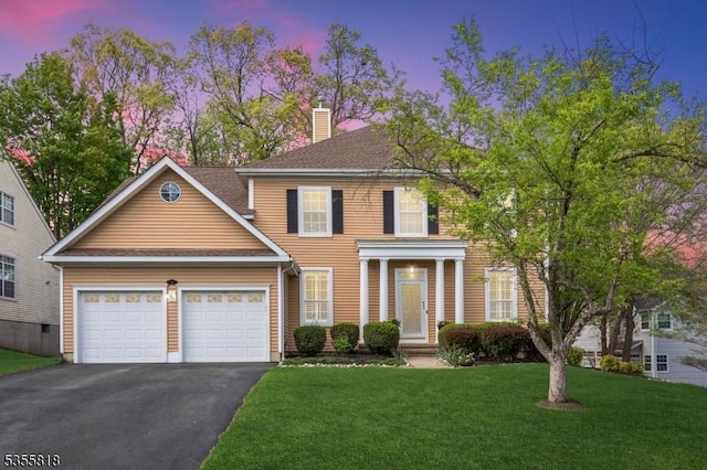 view of front of house featuring an attached garage, a front lawn, a chimney, and driveway