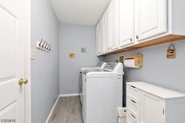 clothes washing area with cabinet space, washing machine and clothes dryer, light wood-type flooring, and baseboards