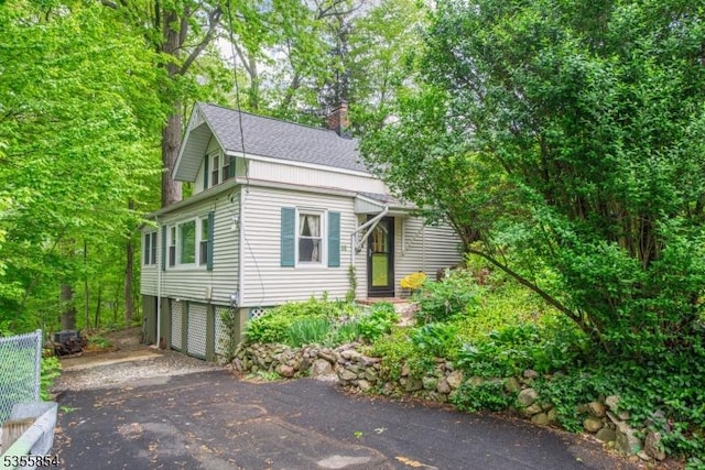 view of side of home featuring roof with shingles, a chimney, an attached garage, and driveway