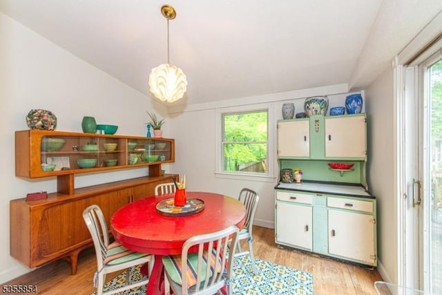 dining area with light wood finished floors, baseboards, and vaulted ceiling