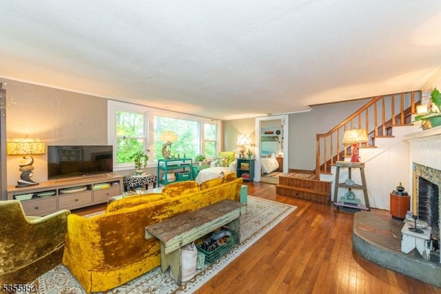 living room with wood-type flooring, stairs, and a fireplace with raised hearth