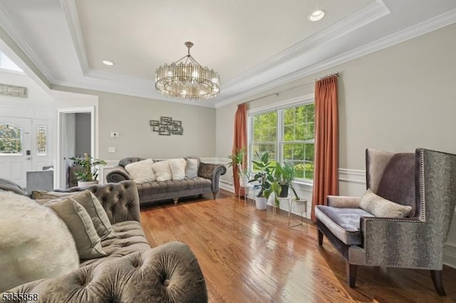 living area with a tray ceiling, wood finished floors, a chandelier, and crown molding