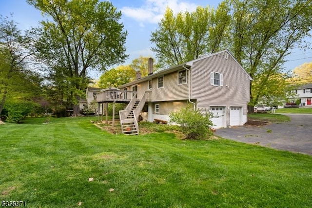 rear view of house featuring stairs, a chimney, driveway, a wooden deck, and a garage