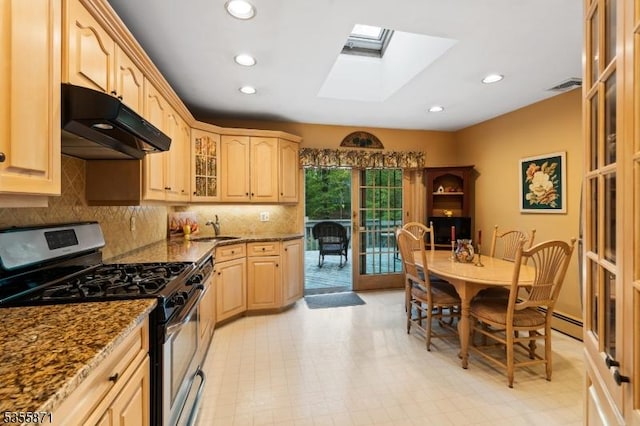 kitchen with stainless steel range with gas stovetop, under cabinet range hood, a sink, light brown cabinets, and dark stone countertops