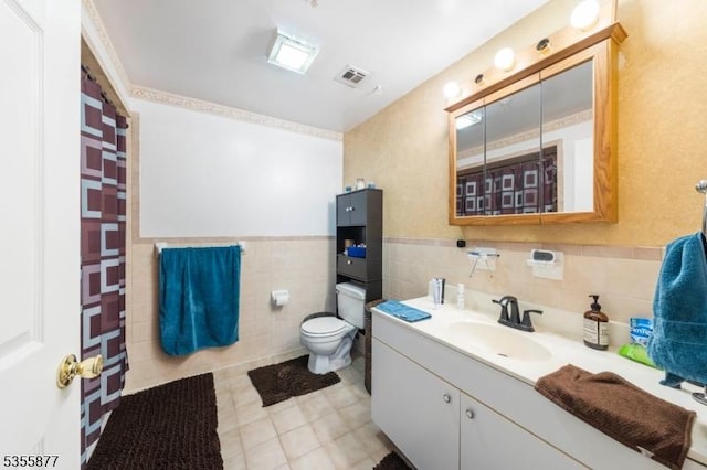 full bathroom with tile walls, toilet, vanity, tile patterned floors, and a wainscoted wall