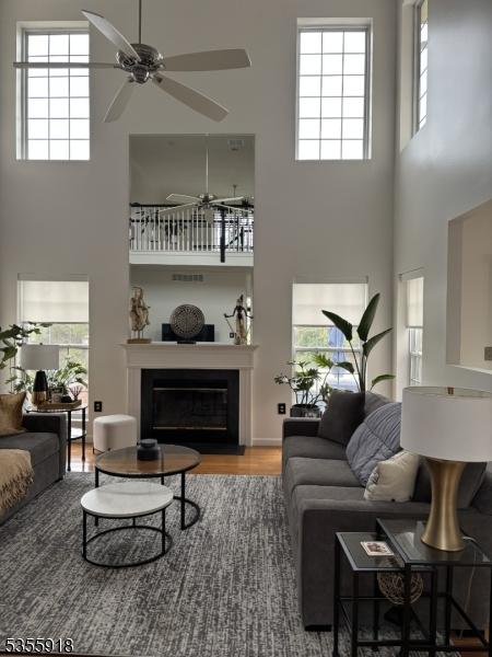 living room featuring a towering ceiling, a ceiling fan, wood finished floors, a glass covered fireplace, and plenty of natural light